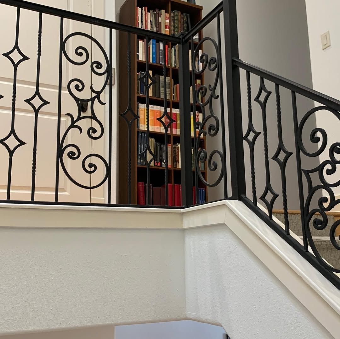 Wrought-iron staircase railing beside a bookshelf in a bright home interior