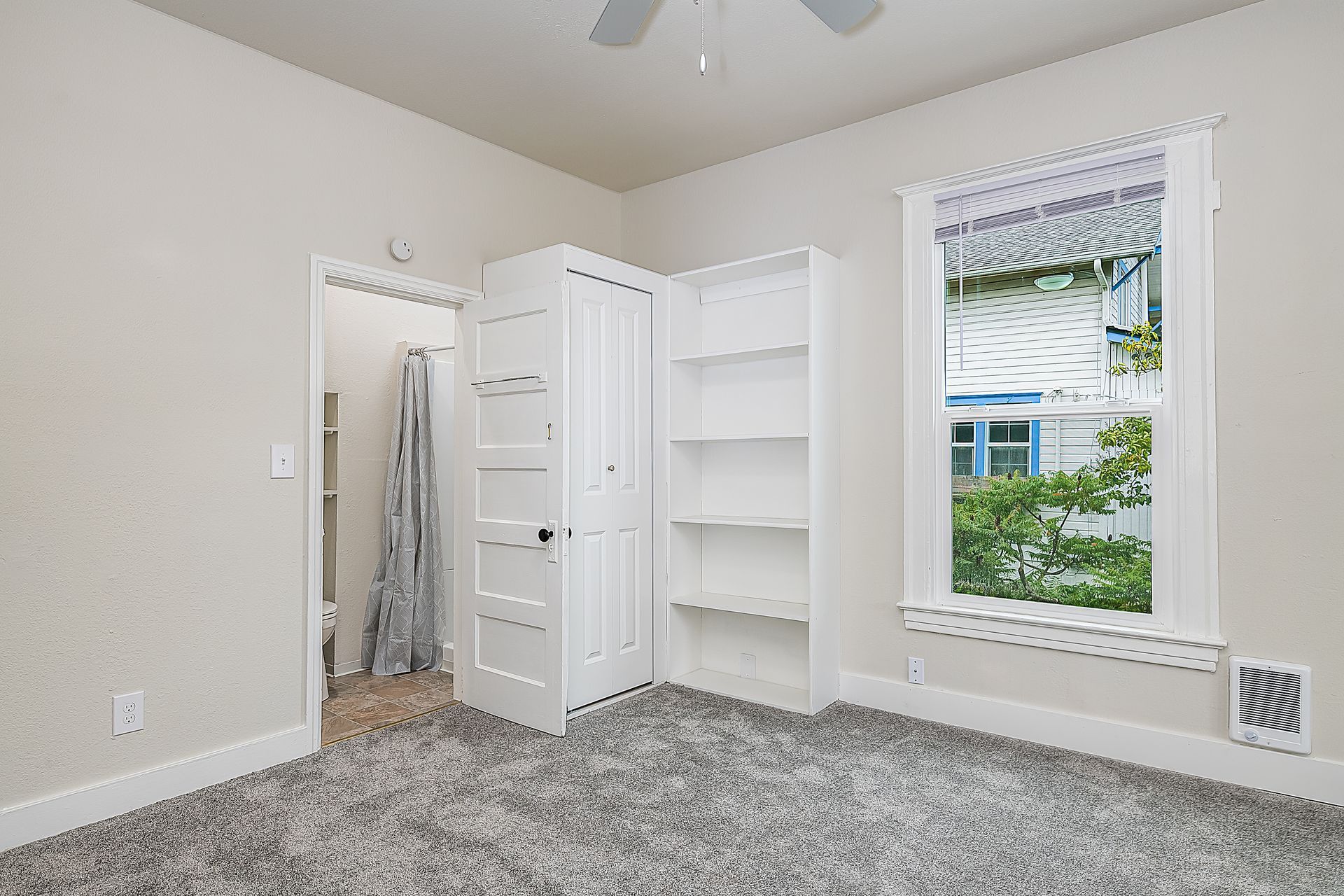 Photo of a bedroom with a tall window, ceiling fan, and more