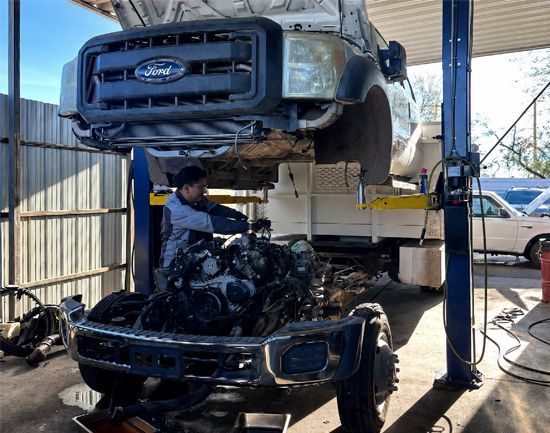 Mechanic working under a raised Ford truck in an auto repair shop