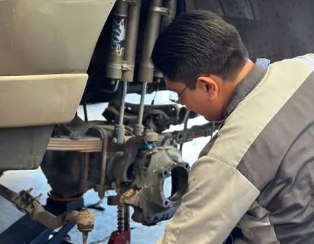 Mechanic inspecting a vehicle’s exposed rear wheel assembly with tools in a garage