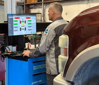 Mechanic using a computer at an auto repair station beside a maroon vehicle