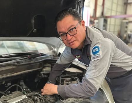 Mechanic in gray shirt working under the hood of a car in a garage