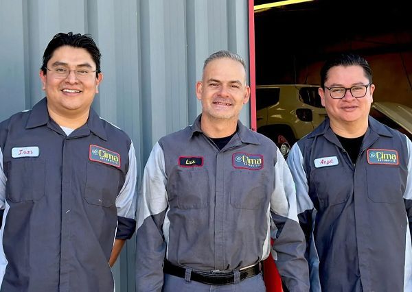 Three men in gray work uniforms standing together in front of a garage opening