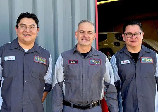Three men in gray work uniforms standing together in front of a garage opening