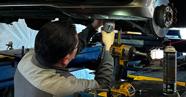 Mechanic working under a car with power tools in a garage repair bay