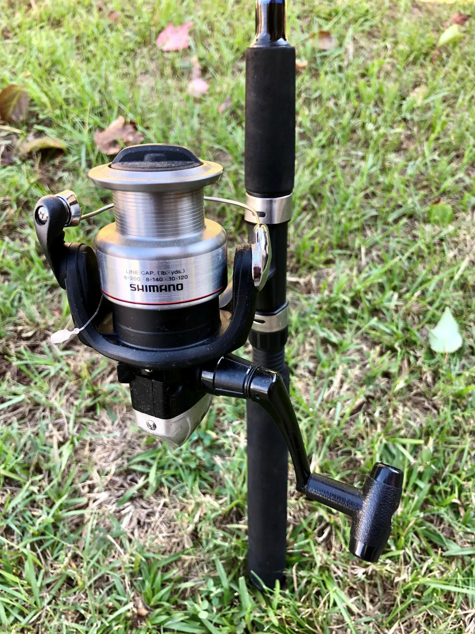 Fishing reel mounted on a black rod holder in grass