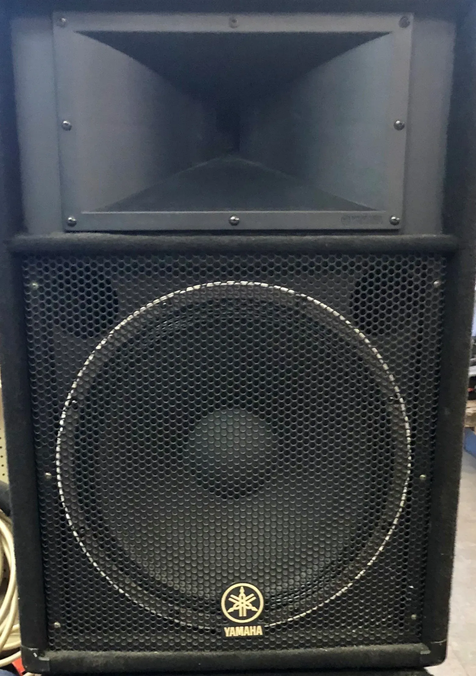 Black speaker cabinet with a large woofer and horn on top against a dark background