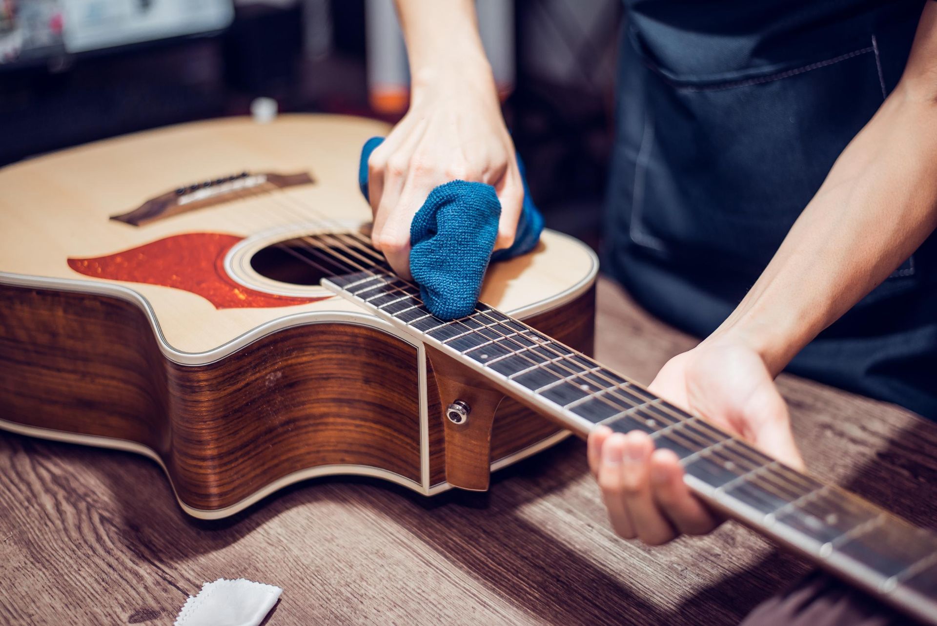 Person cleaning a wooden acoustic guitar with a blue cloth on a table