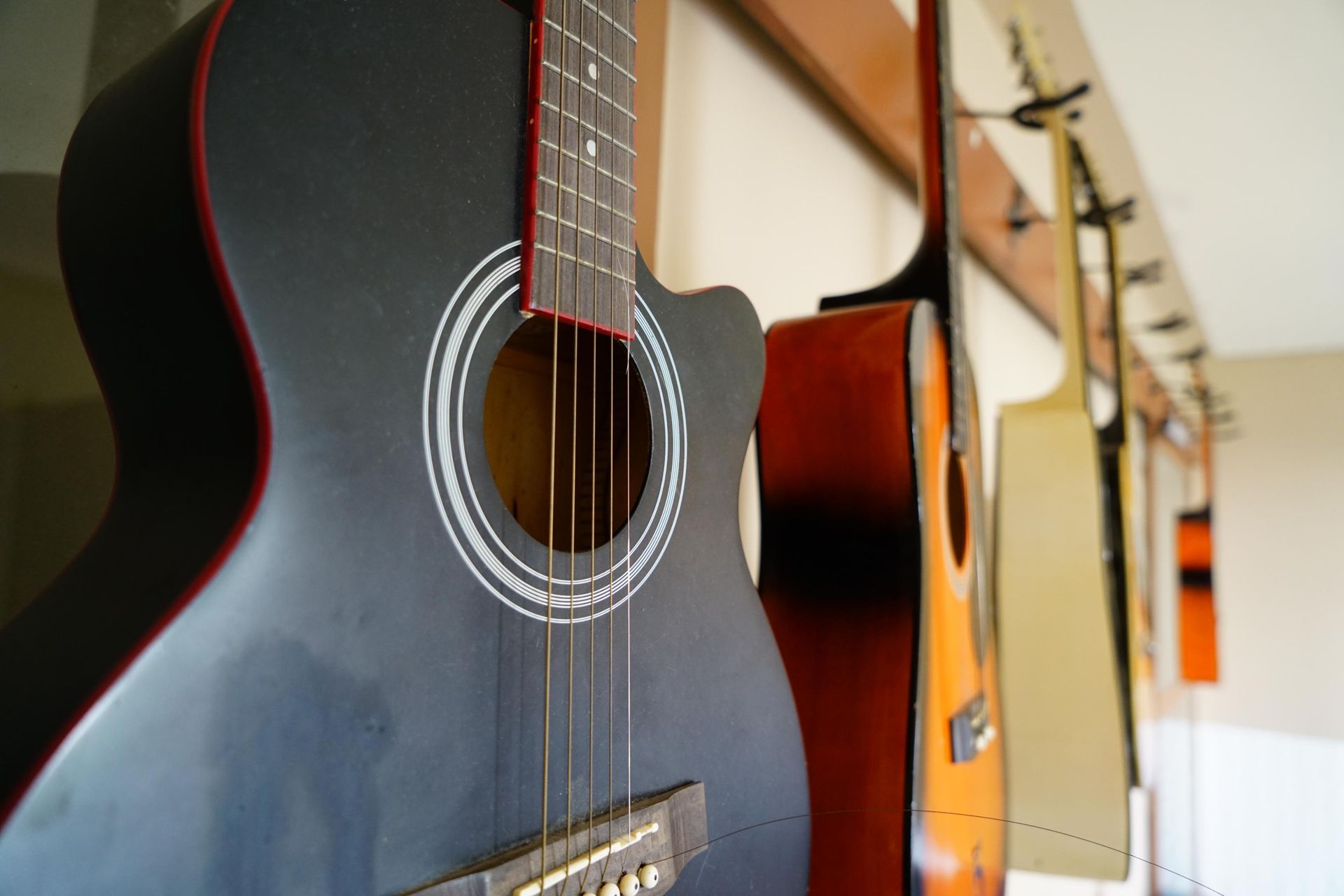 Several acoustic guitars hanging on a wall, including a black and a sunburst guitar, in a music shop.