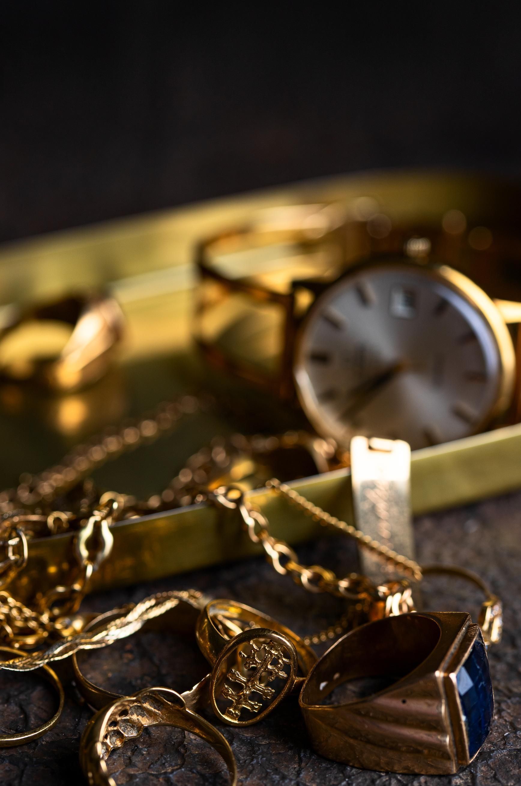 Gold watch and jewelry on a dark surface, with a brown striped pendant in the foreground