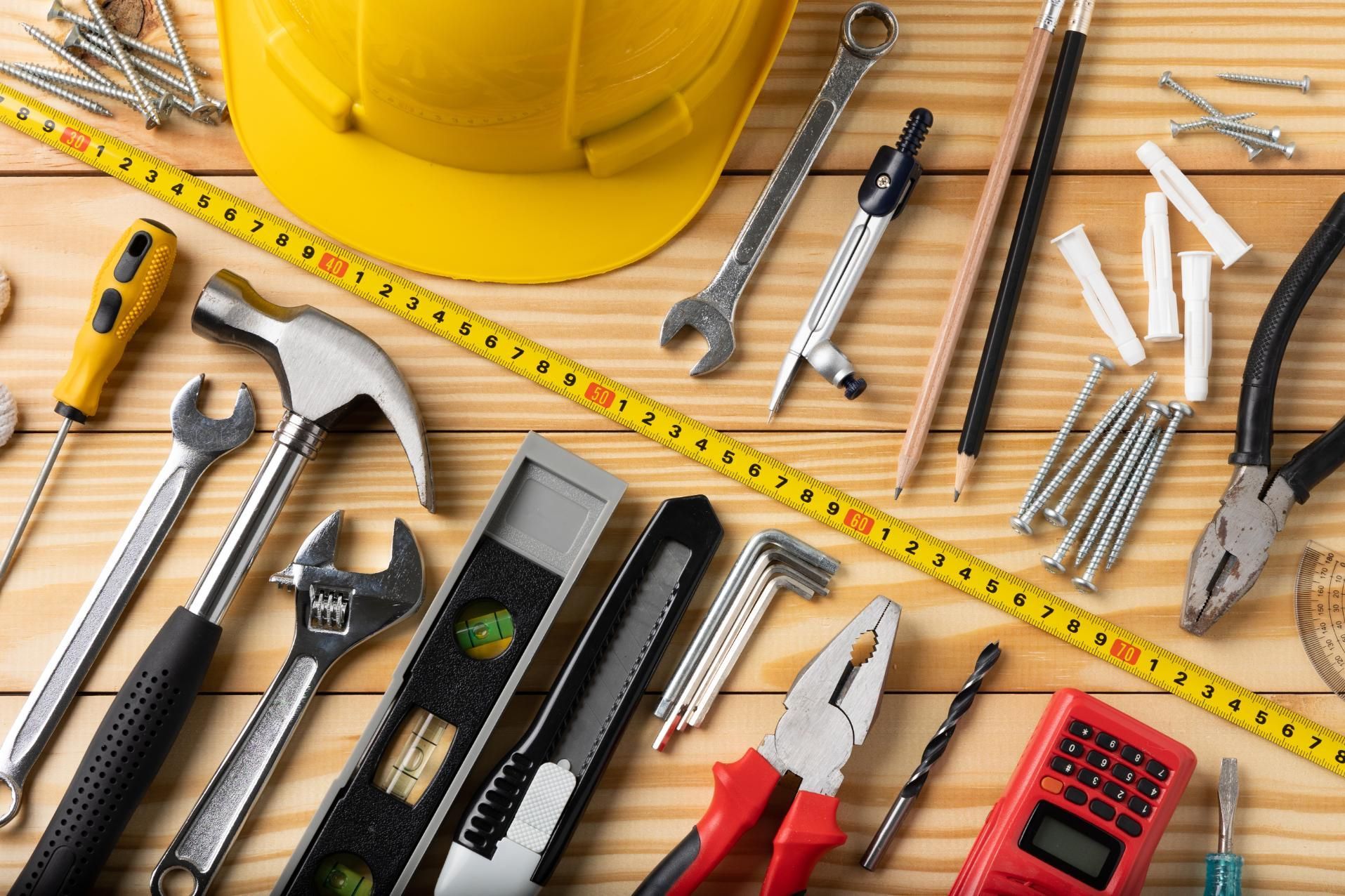 Yellow hard hat with assorted tools and measuring tape on a wooden workbench