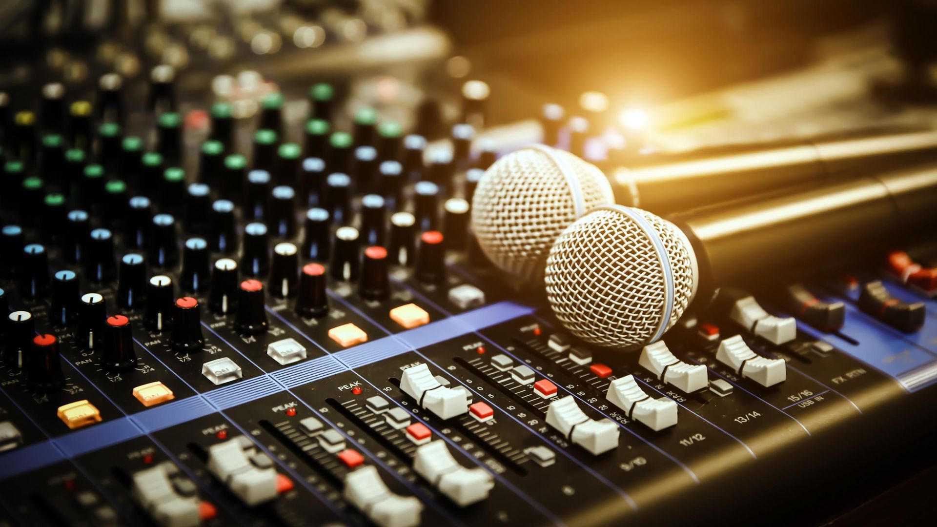 Two microphones on a colorful audio mixing console with sliders and glowing lights
