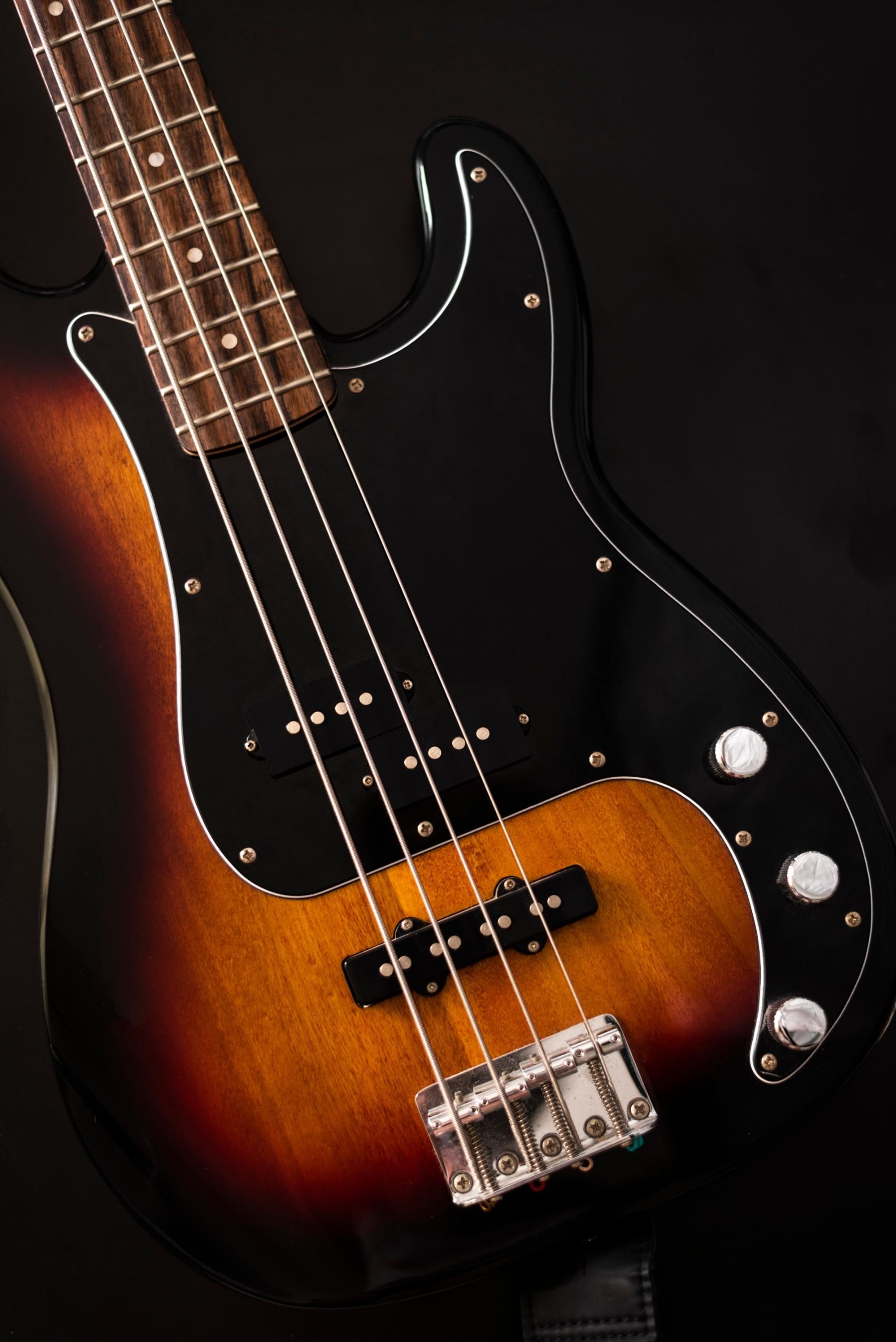 Sunburst electric bass guitar with black pickguard on a black background