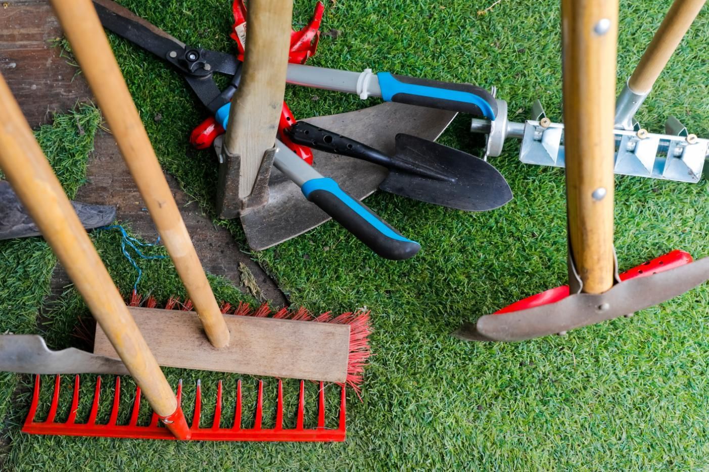 Gardening tools on grass: rakes, spade, shovel, and shears leaning against wooden handles