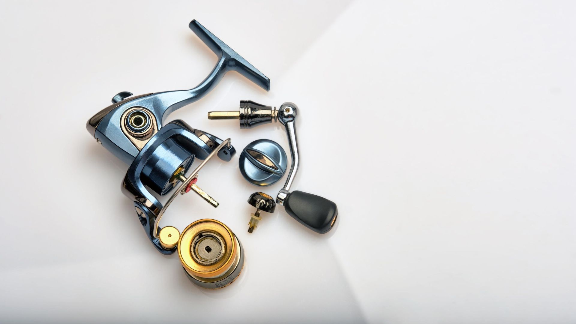 Assorted metallic mechanical parts and tools on a white surface, including a reel, screws, and a handle