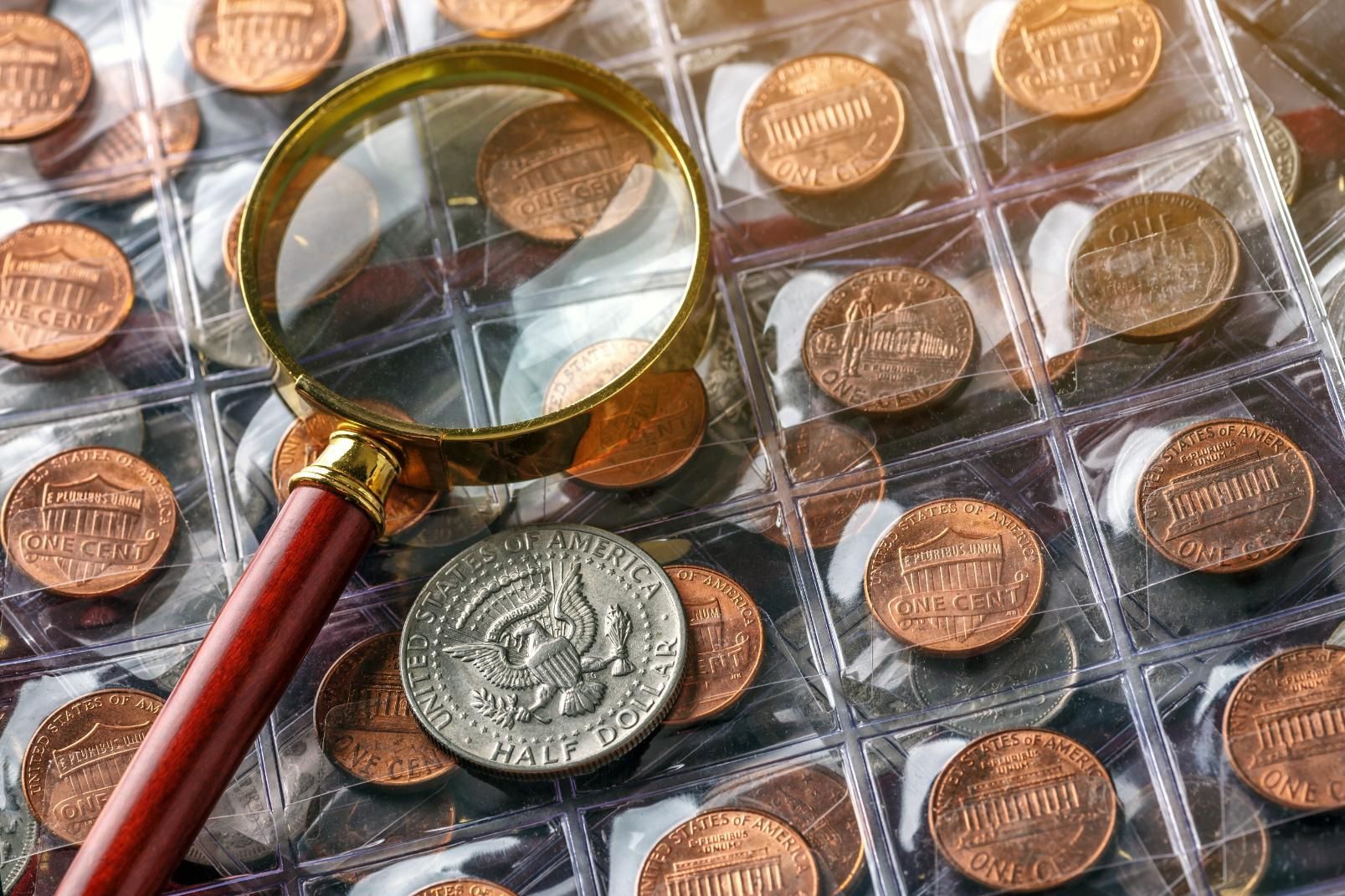 Magnifying glass over a collection of coins in plastic sleeves, with a large silver coin centered nearby