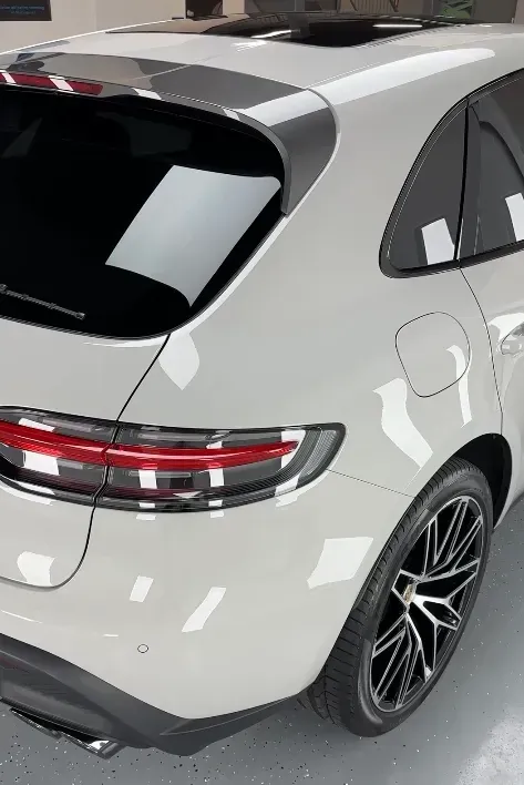 A white car with black wheels is parked in a garage with new ceramic window tinting completed.