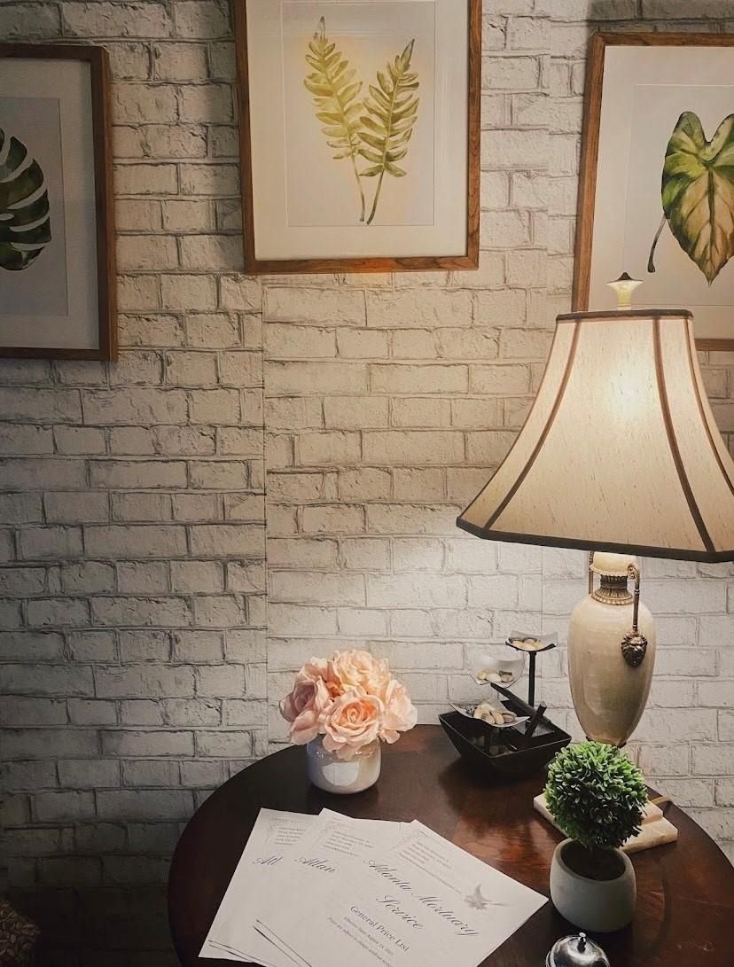 Cozy desk with lamp, papers, flowers, and framed botanical art against a brick wall.