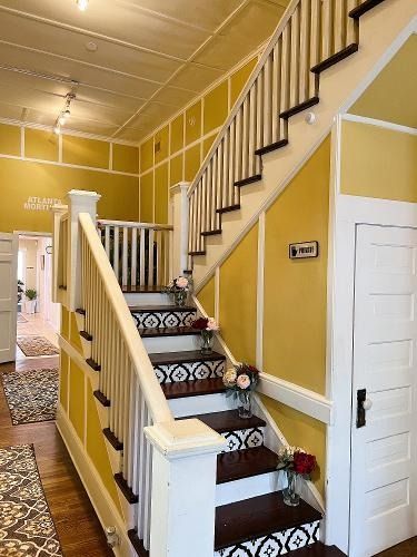 Staircase in a yellow hallway with white railings, patterned carpet, and a closed white door.