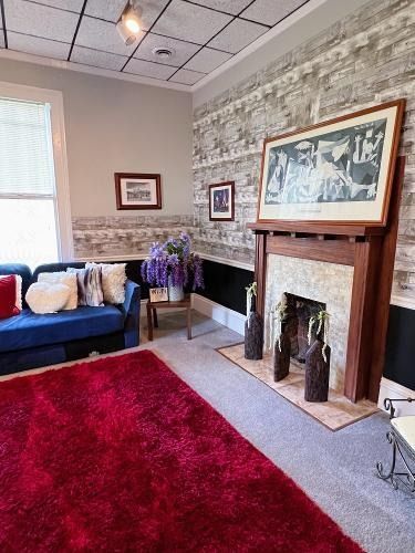 Cozy living room with blue sofa, red rug, fireplace, framed art, and stone-patterned walls