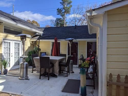 Patio with outdoor dining table, chairs, umbrella, and potted plants beside a house