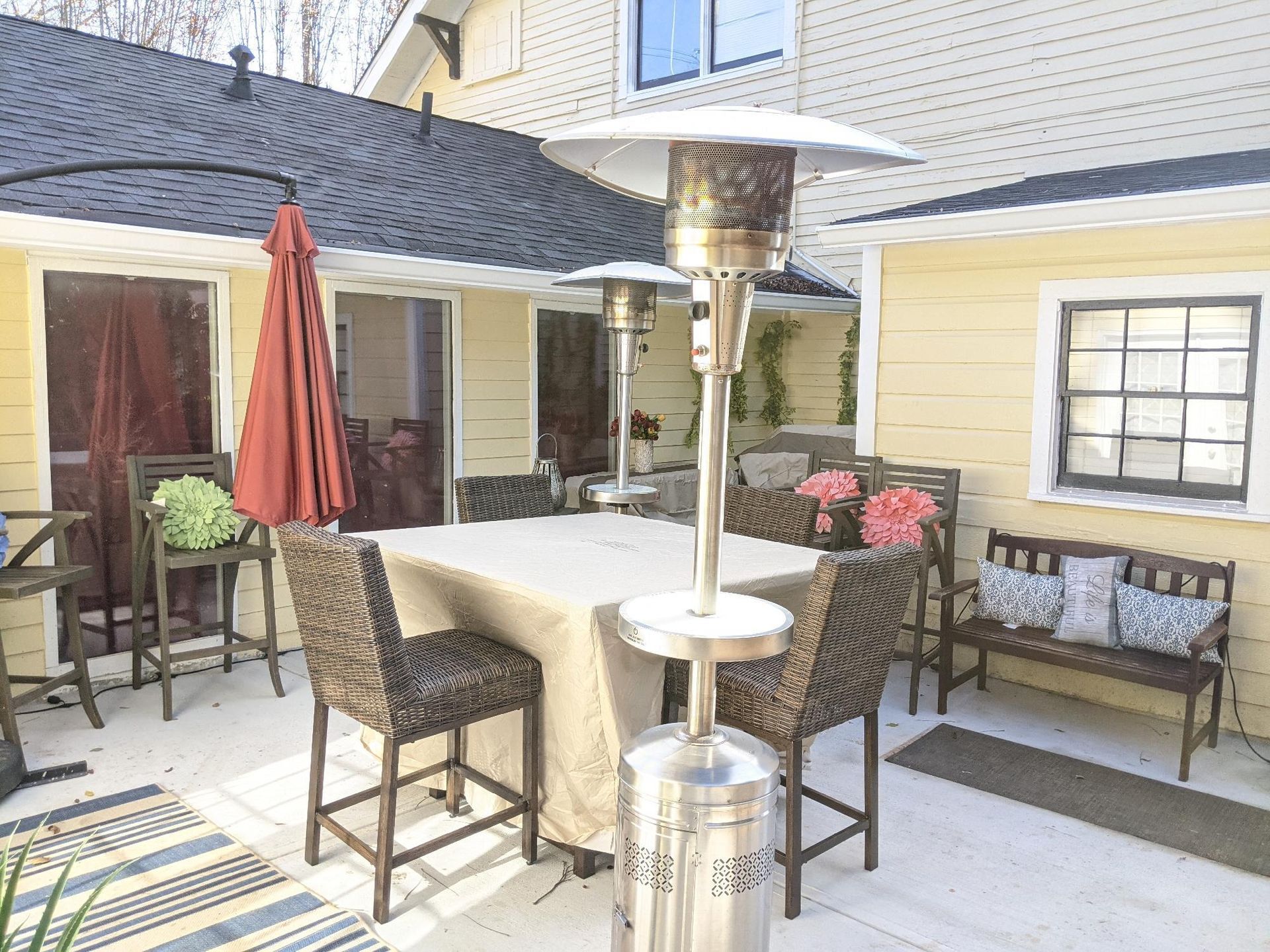 Patio with wicker chairs, table, red umbrella, and patio heater beside a yellow house