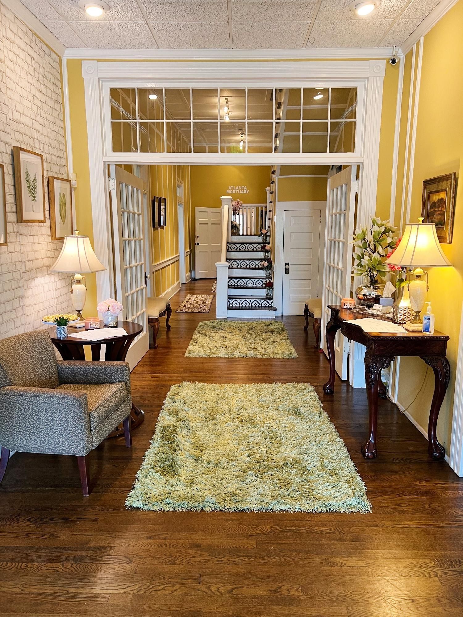 Elegant hallway with hardwood floors, patterned rugs, yellow walls, and a staircase at the far end