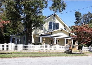 Yellow house with white trim, picket fence, and front porch on a tree-lined street