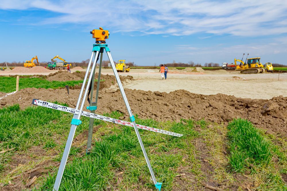 A Tripod Is Sitting In The Middle Of A Field With A Construction Site In The Background — CalCo Surveyors Pty Ltd in Diamond Beach, NSW
