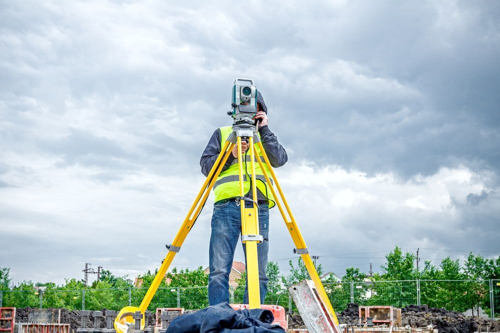 A Man Is Standing On A Tripod Looking Through A Telescope — CalCo Surveyors Pty Ltd in Wingham, NSW