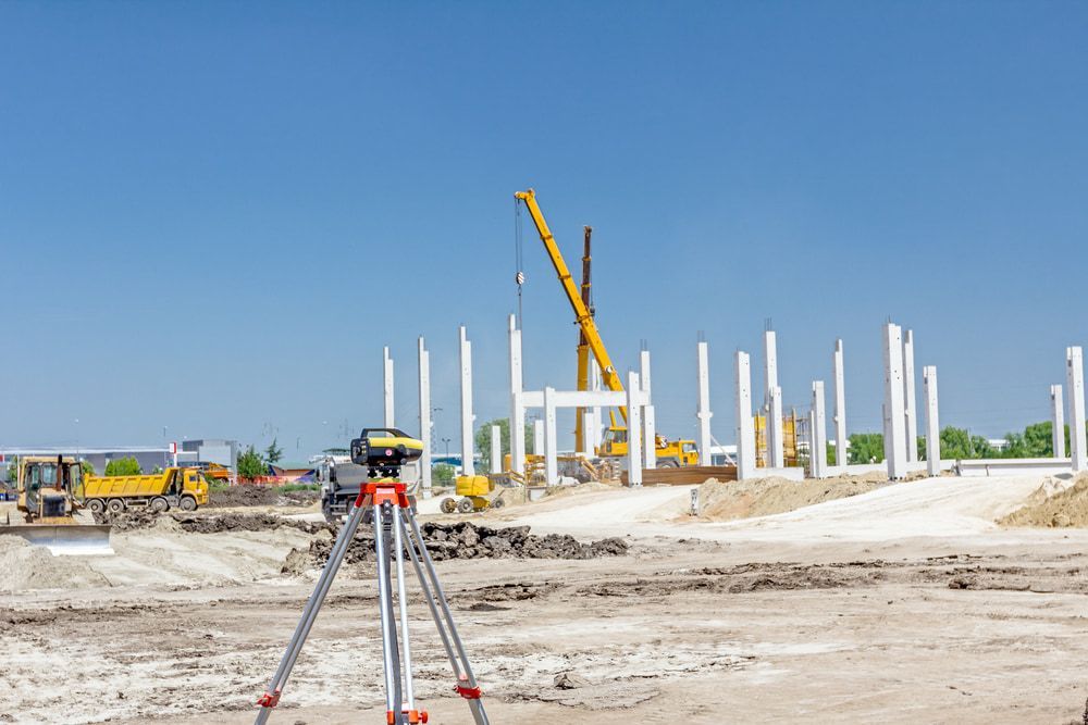 A Construction Site With A Level On A Tripod In The Foreground And A Crane In The Background — CalCo Surveyors Pty Ltd in Harrington, NSW