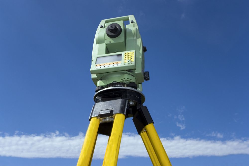 A Green And Yellow Theodolite On A Tripod Against A Blue Sky — CalCo Surveyors Pty Ltd in Gloucester, NSW