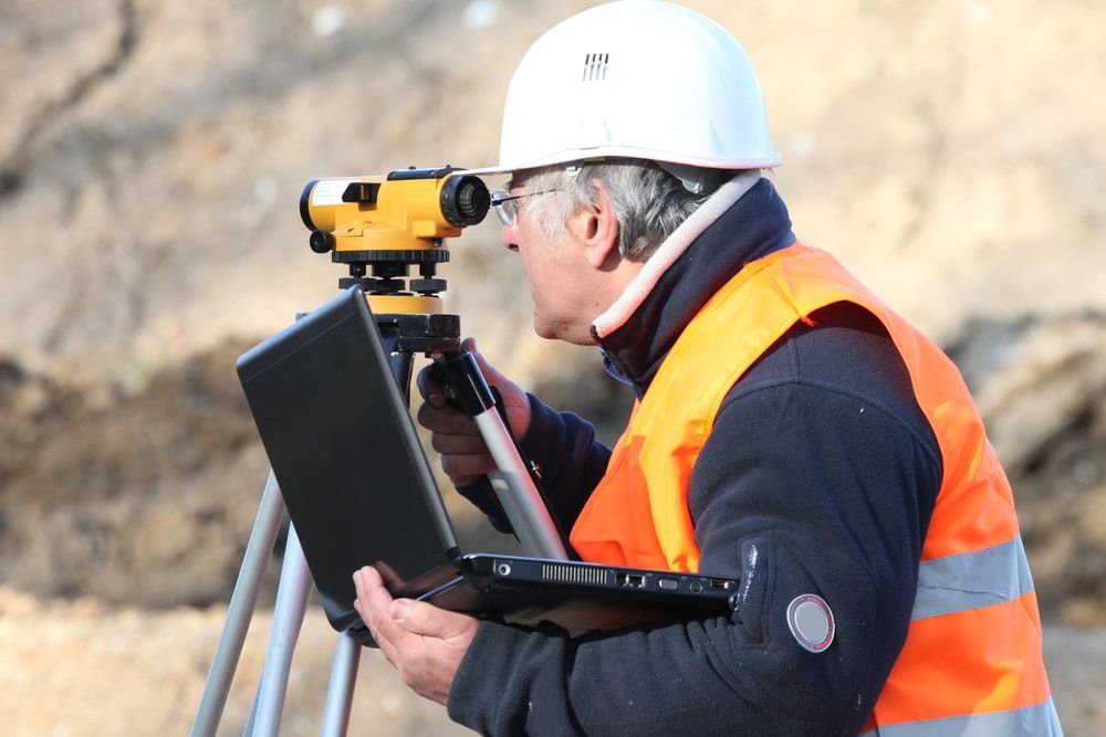 A Man Wearing A Hard Hat Is Looking Through A Telescope While Holding A Laptop — CalCo Surveyors Pty Ltd in Harrington, NSW