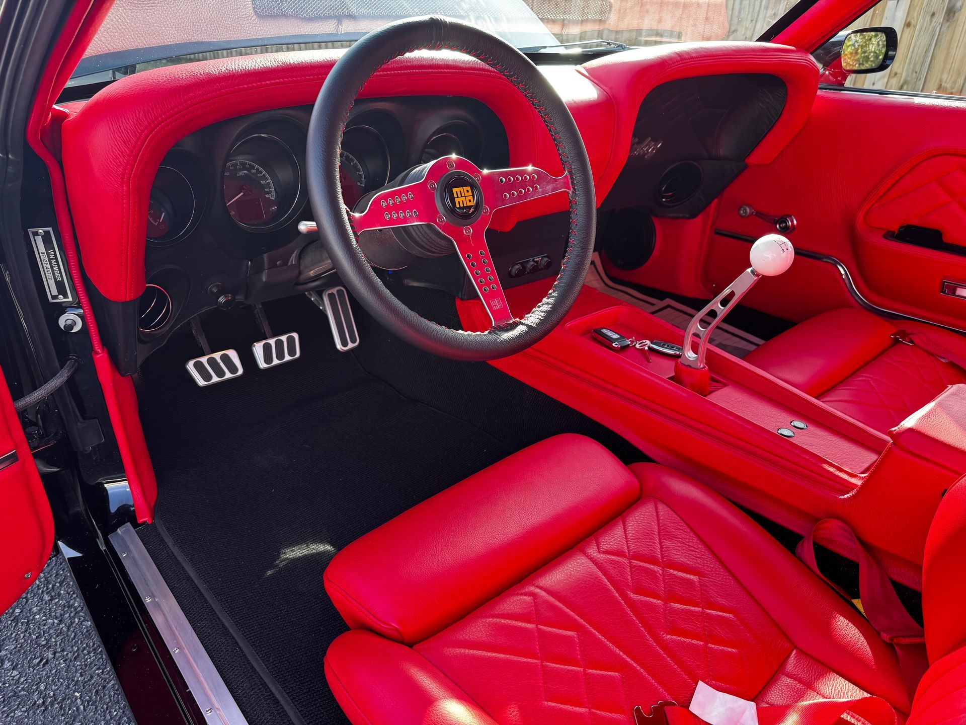 Interior of a custom vintage car featuring bright red leather upholstery, a black steering wheel, and a white gear shift.