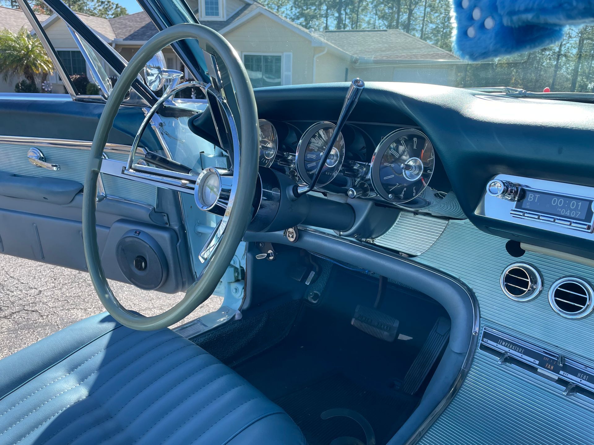 Interior view of a vintage car with blue leather seats, a thin steering wheel, and a chrome-accented dashboard.