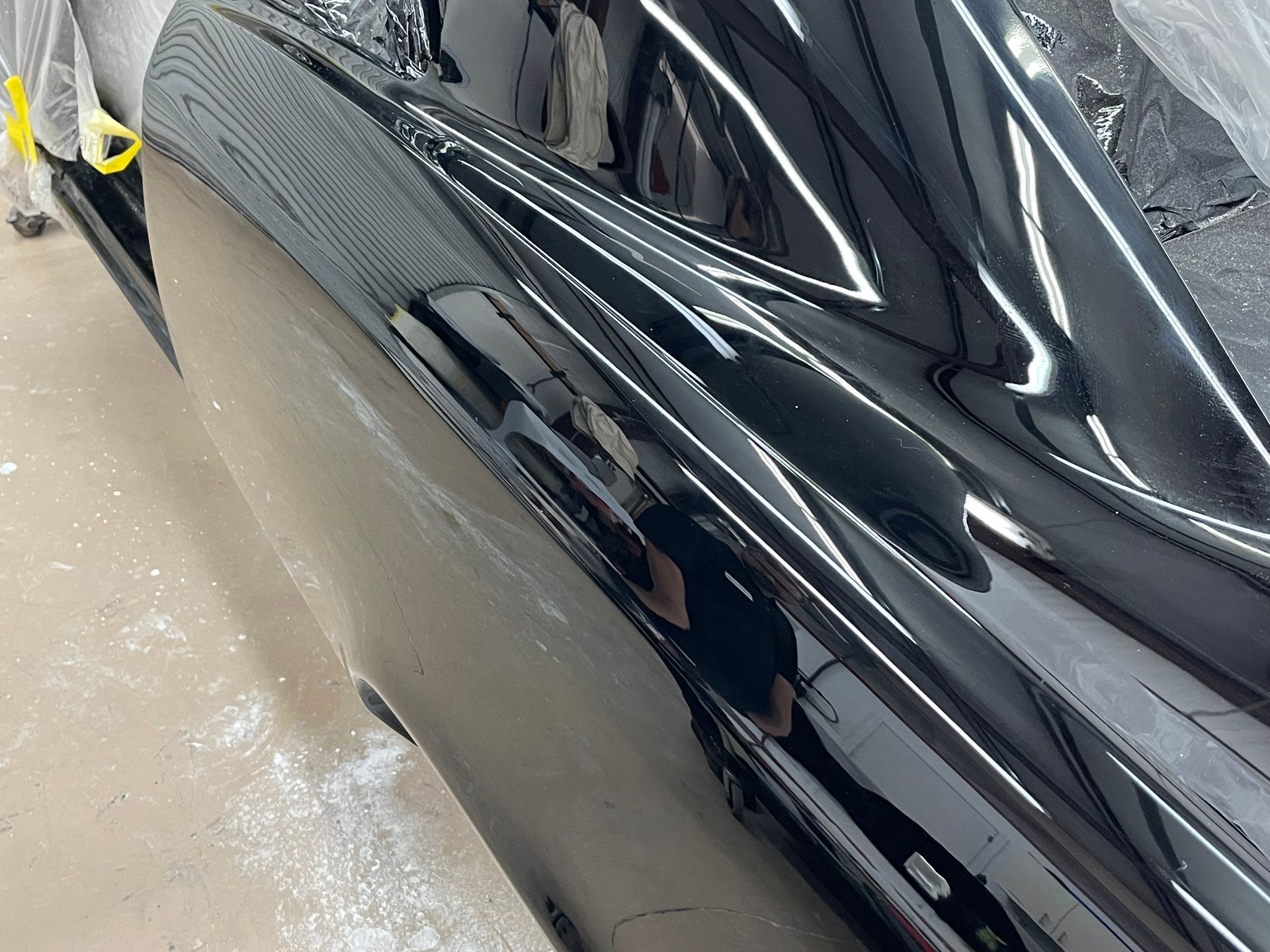 A close-up side view of a glossy, freshly painted black vehicle body in a workshop setting.