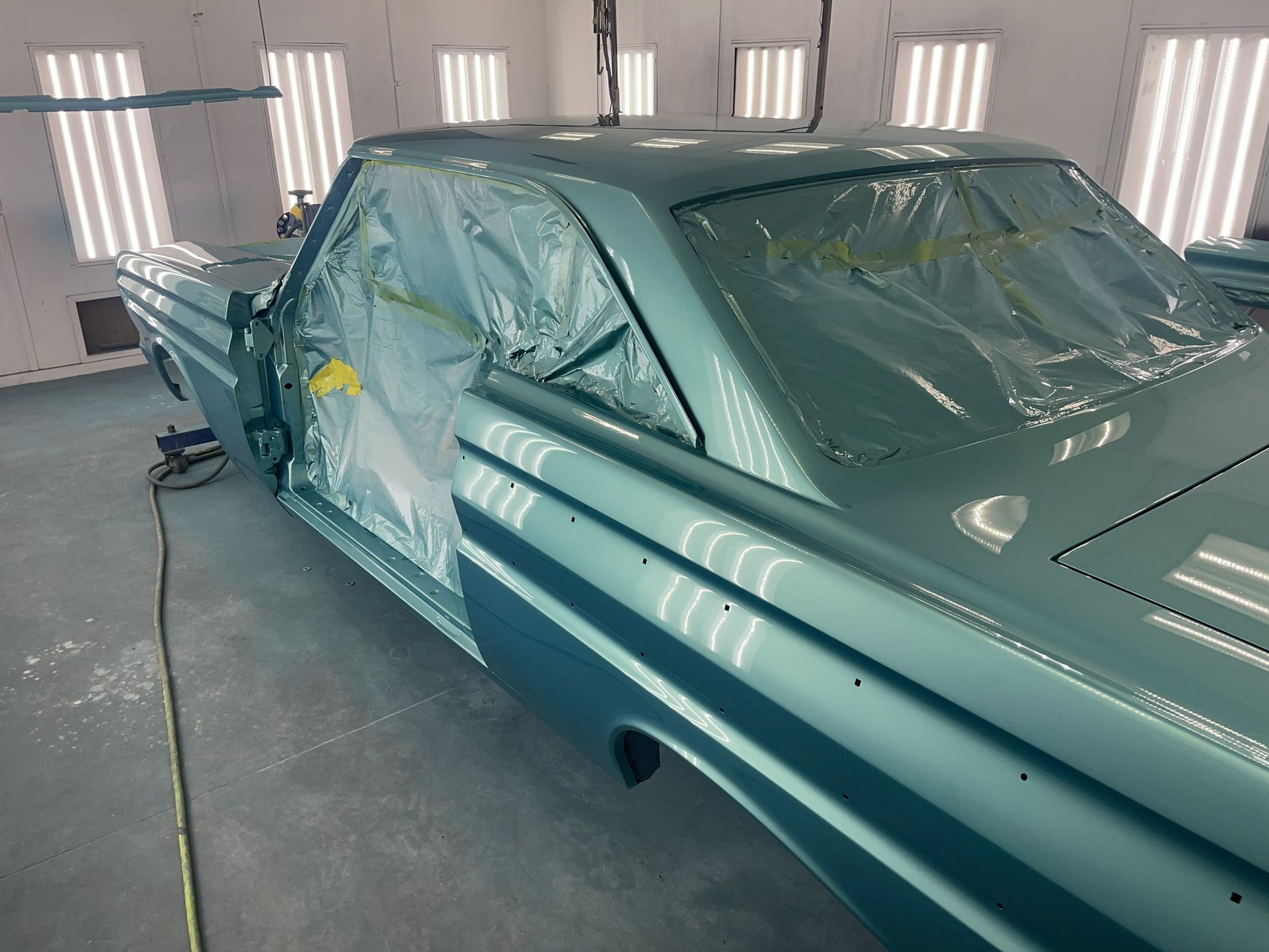 A glossy, light blue vintage car body undergoing a fresh paint job in a well-lit automotive spray booth.