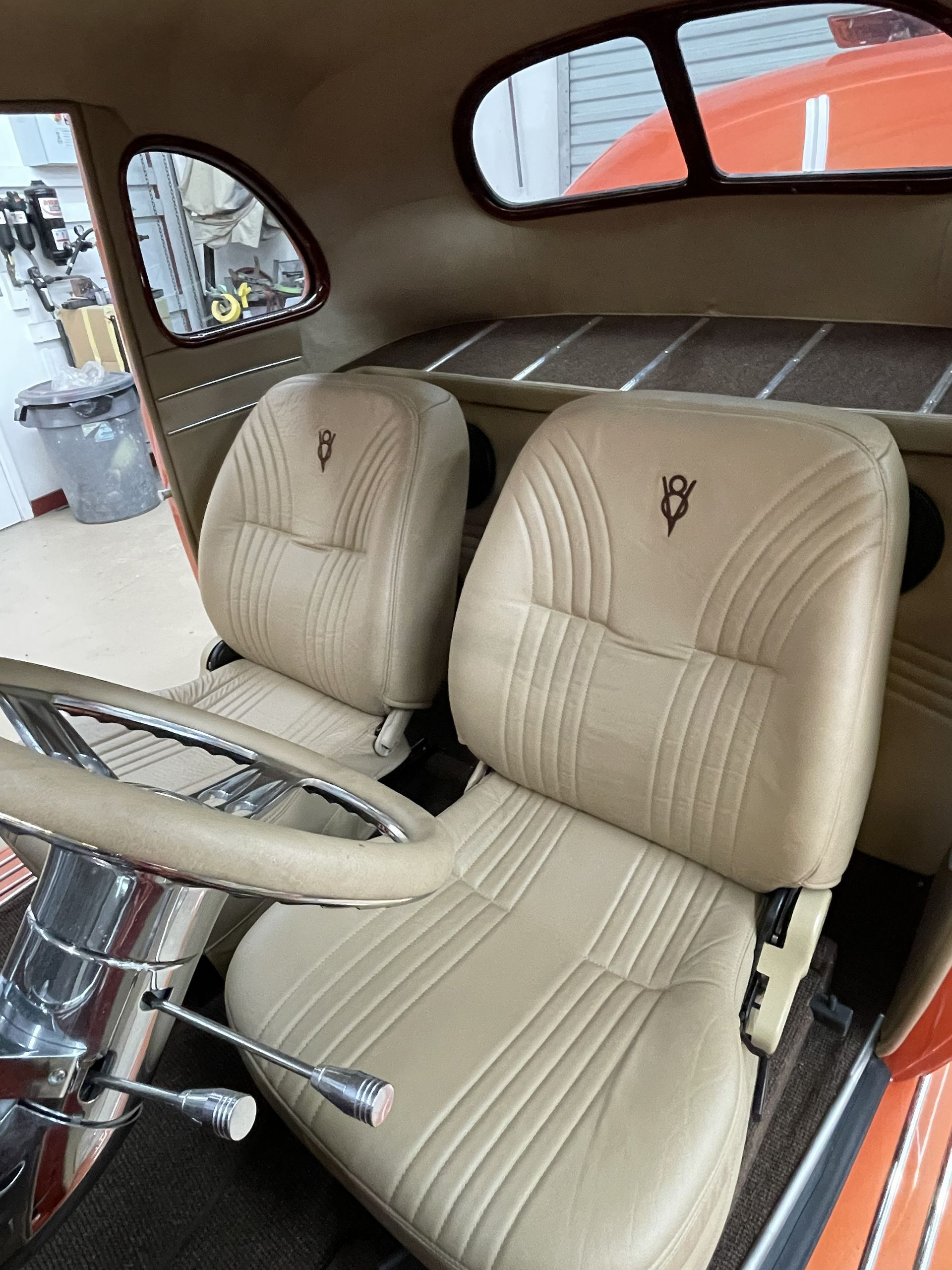 The interior of a classic car featuring two tan leather bucket seats with a V8 emblem stitched into the headrests.