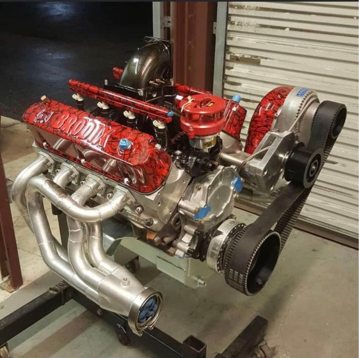 A high-performance V8 engine with red-and-black patterned Brodix valve covers, mounted on a stand in a shop.