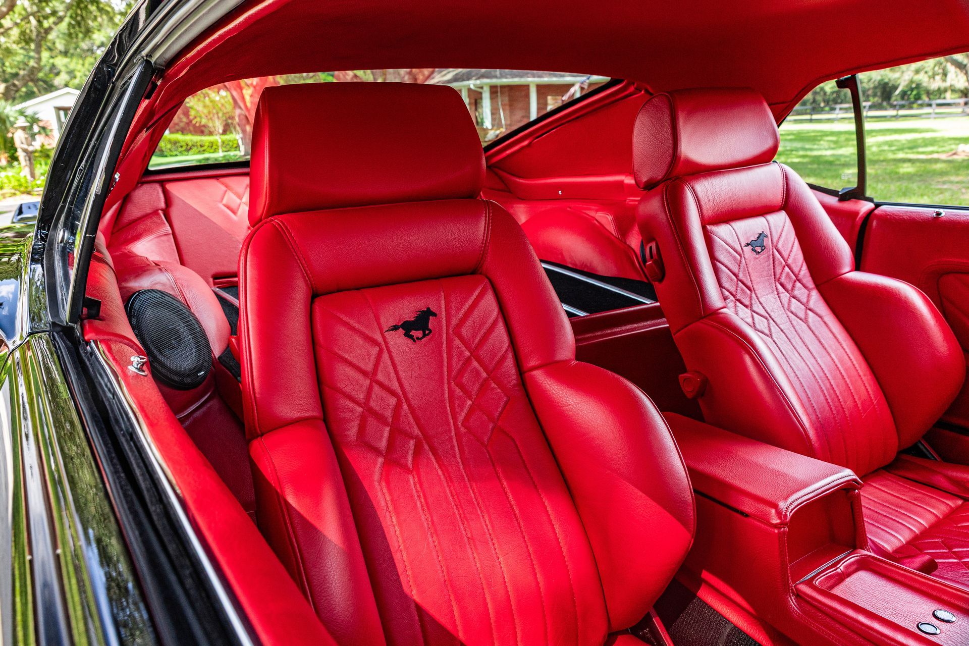Vibrant red leather interior of a classic car, featuring custom stitched bucket seats with a horse emblem.