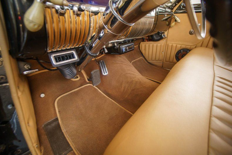Interior view of a classic car with a tan leather bench seat, brown carpet, and a chrome-accented dashboard.
