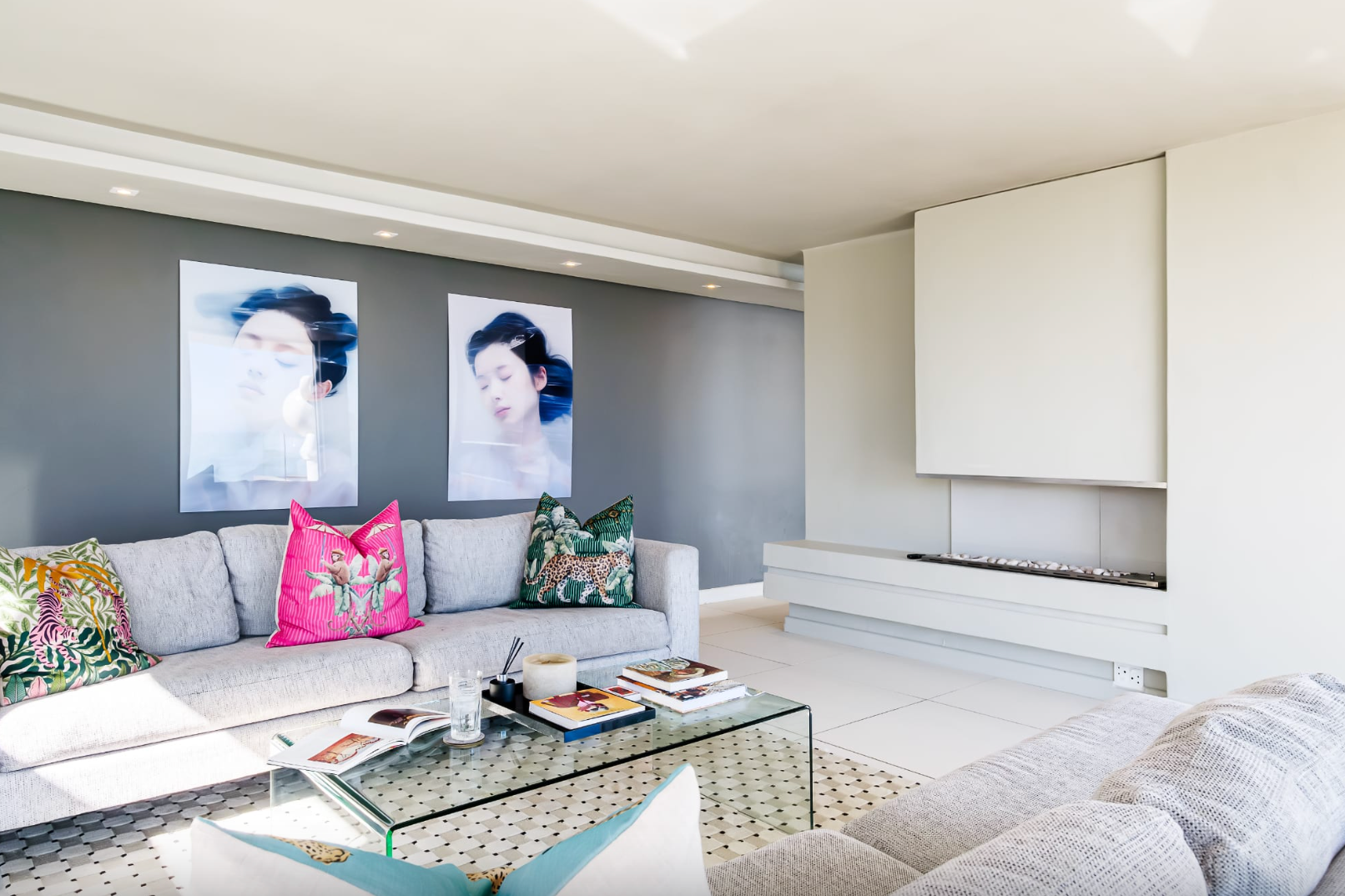 Modern living room with grey walls, white fireplace, and a light-colored sofa with colorful pillows and art.