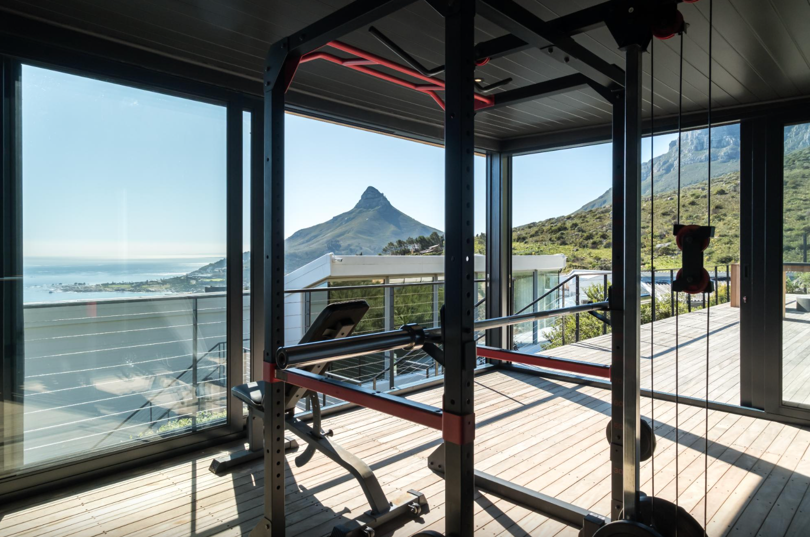 Gym with weightlifting equipment, mountain view through glass walls, sunny day.