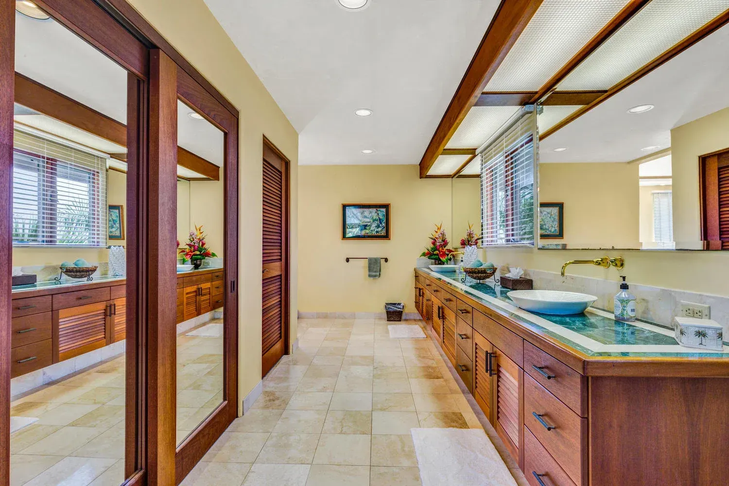 Spacious bathroom with wood cabinetry, large mirrors, beige tile floors, and a long vanity.