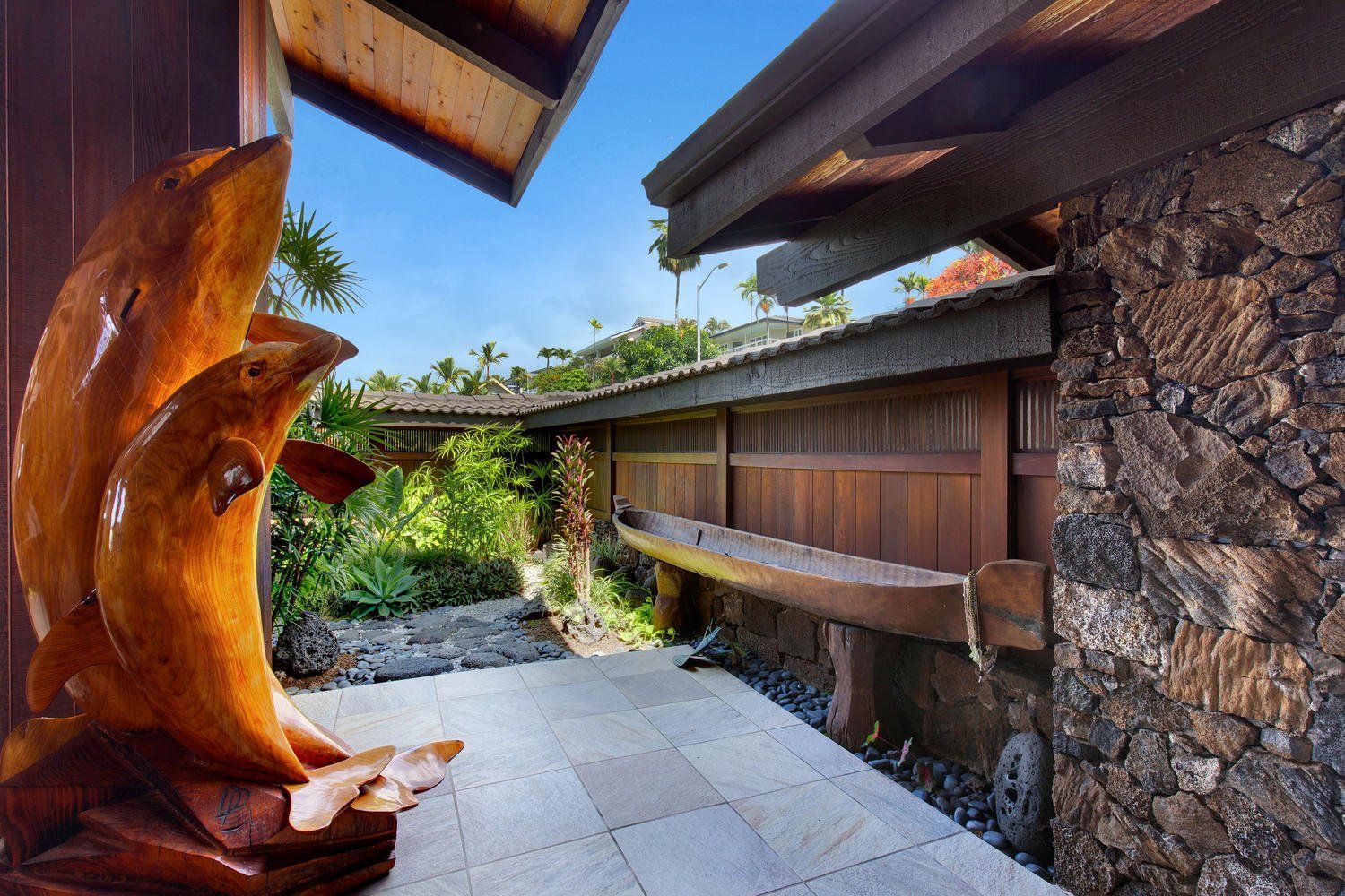 A wooden statue of two dolphins is in front of a stone wall.