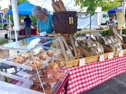 A woman is looking at a display of bread at a farmers market.