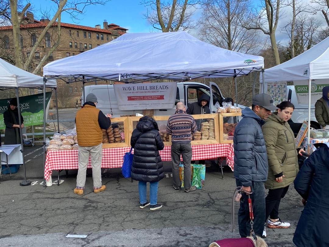 A group of people are standing in front of a food stand with a truck in the background