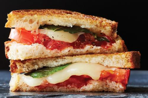 A grilled cheese sandwich with tomatoes and cheese is stacked on top of each other on a table.