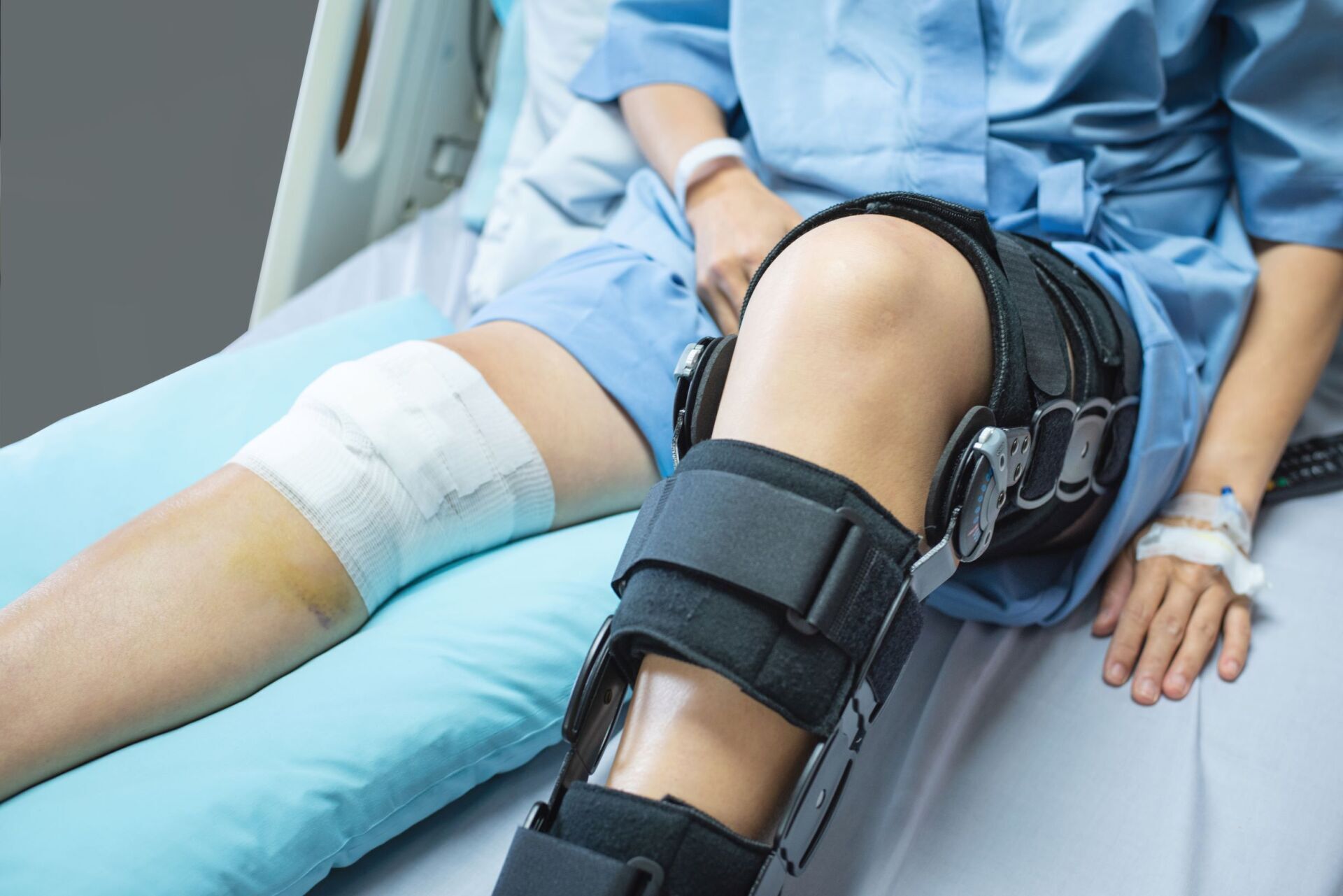Paziente in un letto d'ospedale con una gamba fasciata e un tutore nero al ginocchio.