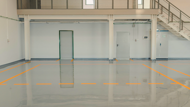 Empty beige room with glossy gray floor, white doors, and a small stack of chairs in the back.